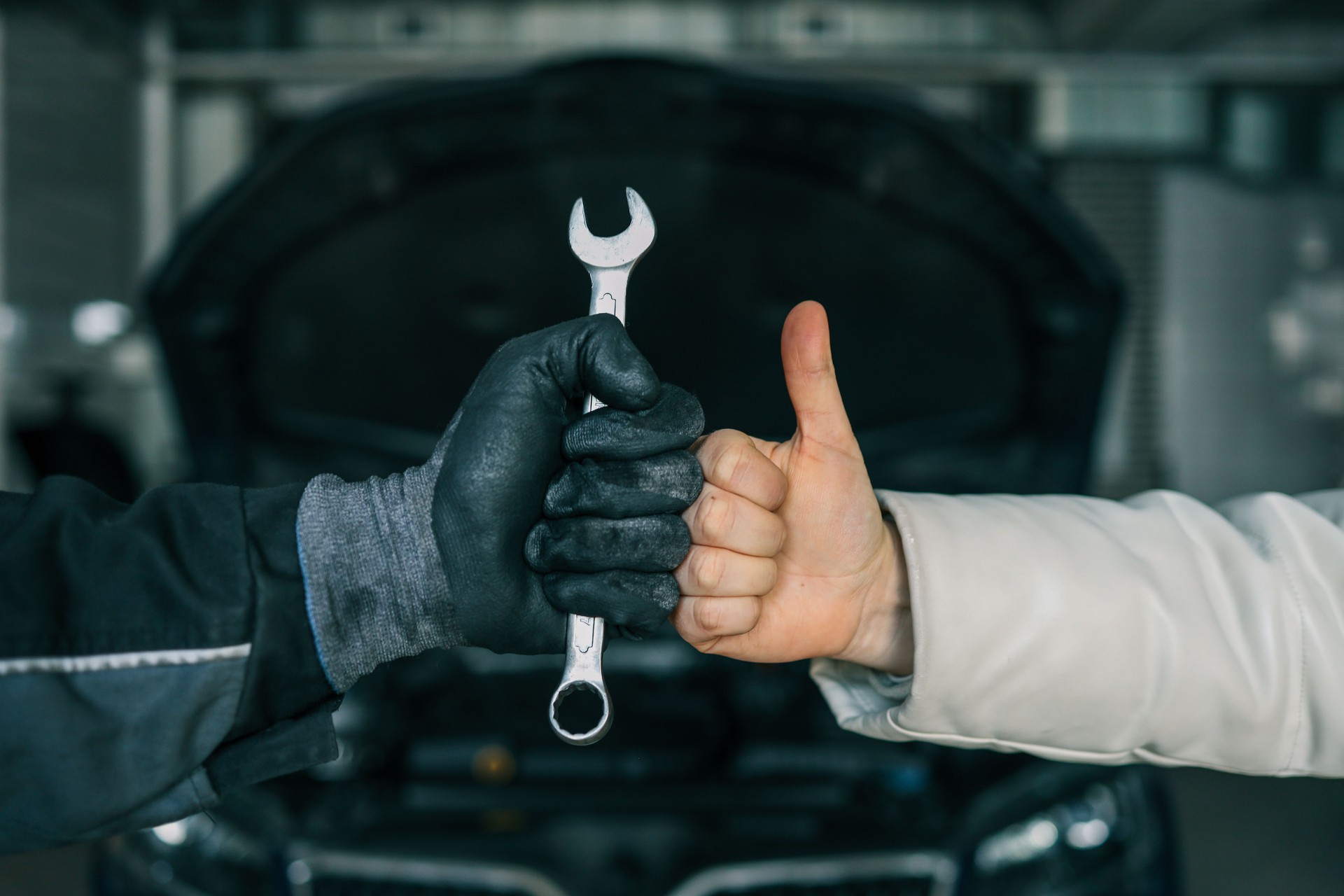 Close-up of a mechanic's gloved hand holding a wrench and a customer's hand giving a thumbs-up, symbolizing satisfaction and trust in car repair services